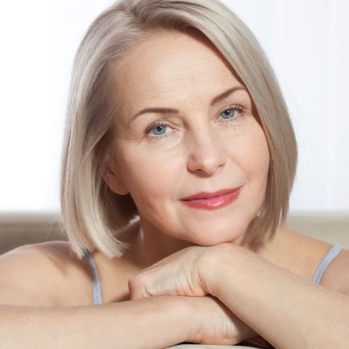 An older woman with short blond hair and blue eyes looks happy and content.