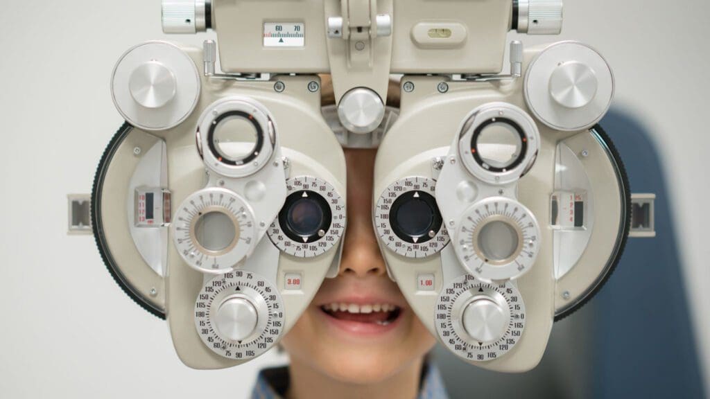 Collins Vision offers children’s eye exams and can diagnose pediatric myopia Young child getting an eye exam by an optician using a phoropter.