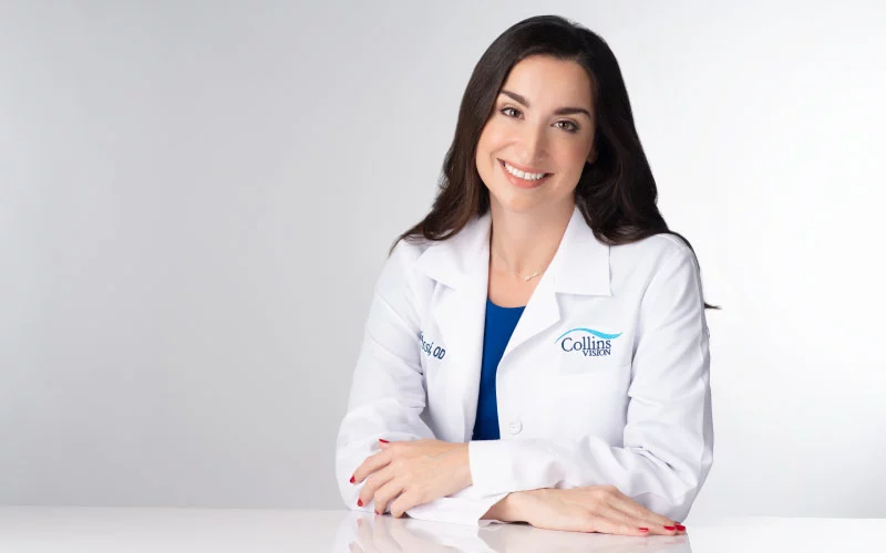Dr. Nicole Alessi sits at a table in her white coat at Collins Vision in Florida